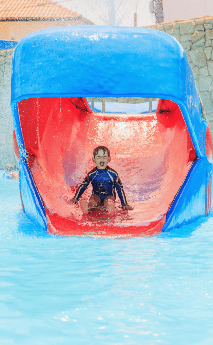 Uma criança com um lindo sorriso e muito alegre pois está escorregando na língua de uma baleia de brinquedo no playground aquático infantil 