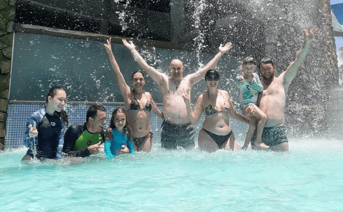 Uma família inteira se divertindo ao se banhar nas águas de uma cascata. Esposo, esposa, pai, mãe, filho, filha, sogro, sogra e sobrinhos.