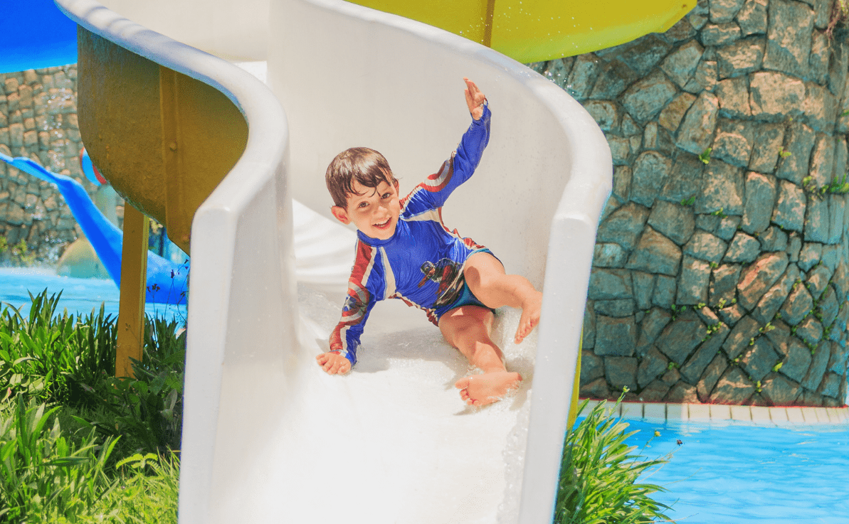 Um criança super feliz escorregando em um toboágua infantil do playground aquático